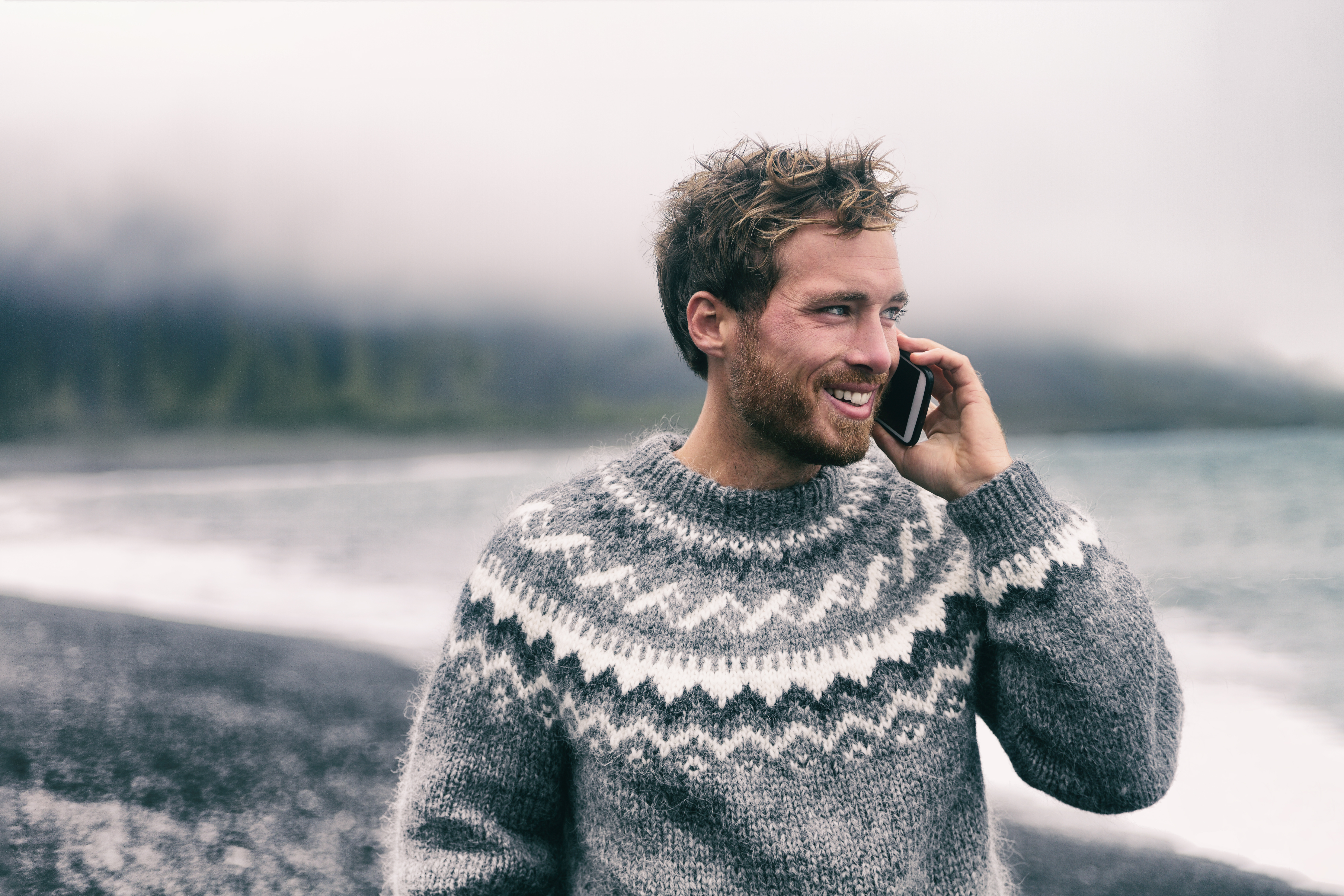 Mies puhuu älypuhelimella talvipuserossa kävelemässä mustalla hiekkarannalla Islannissa.