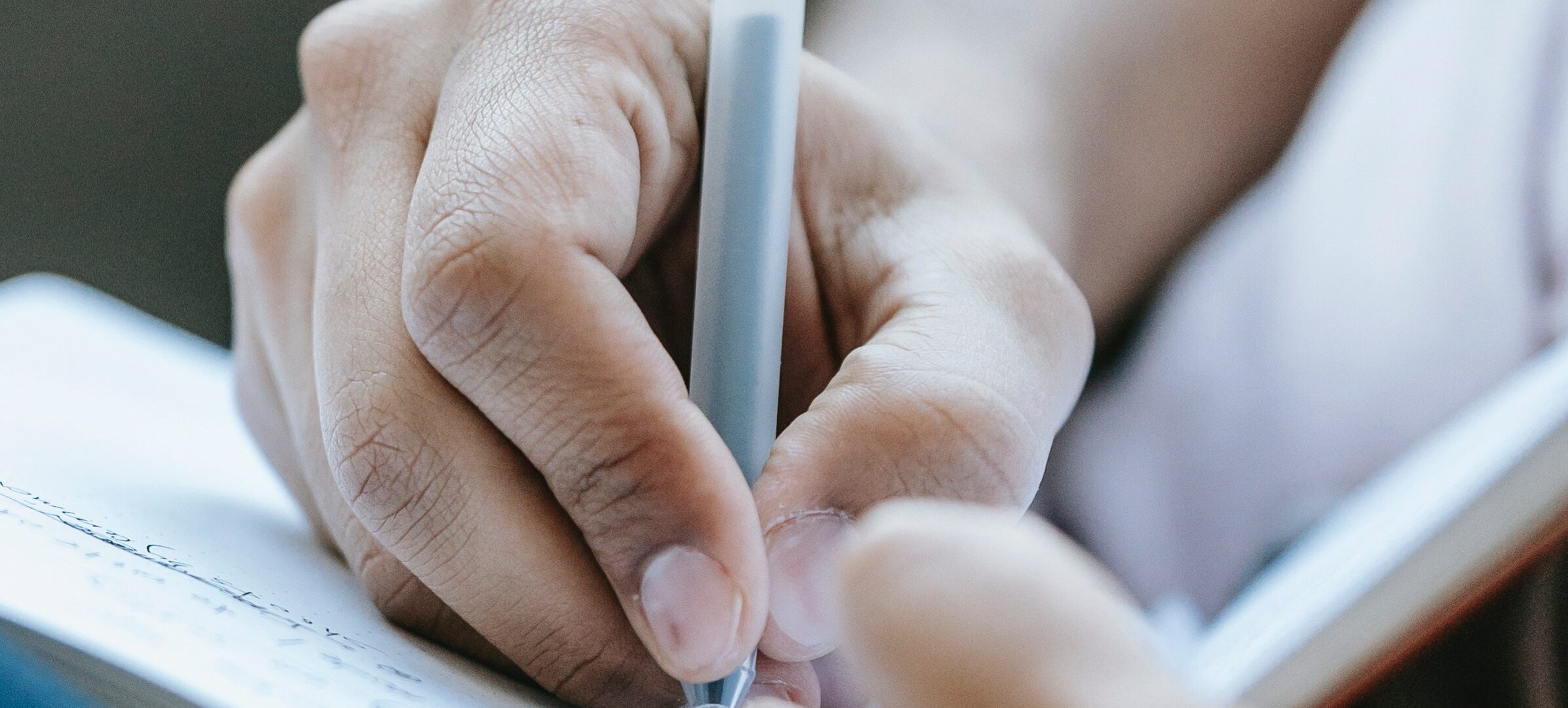 Lähikuva käsi kirjoittaa kuulakärkikynällä kirjaan muistiinpanoja